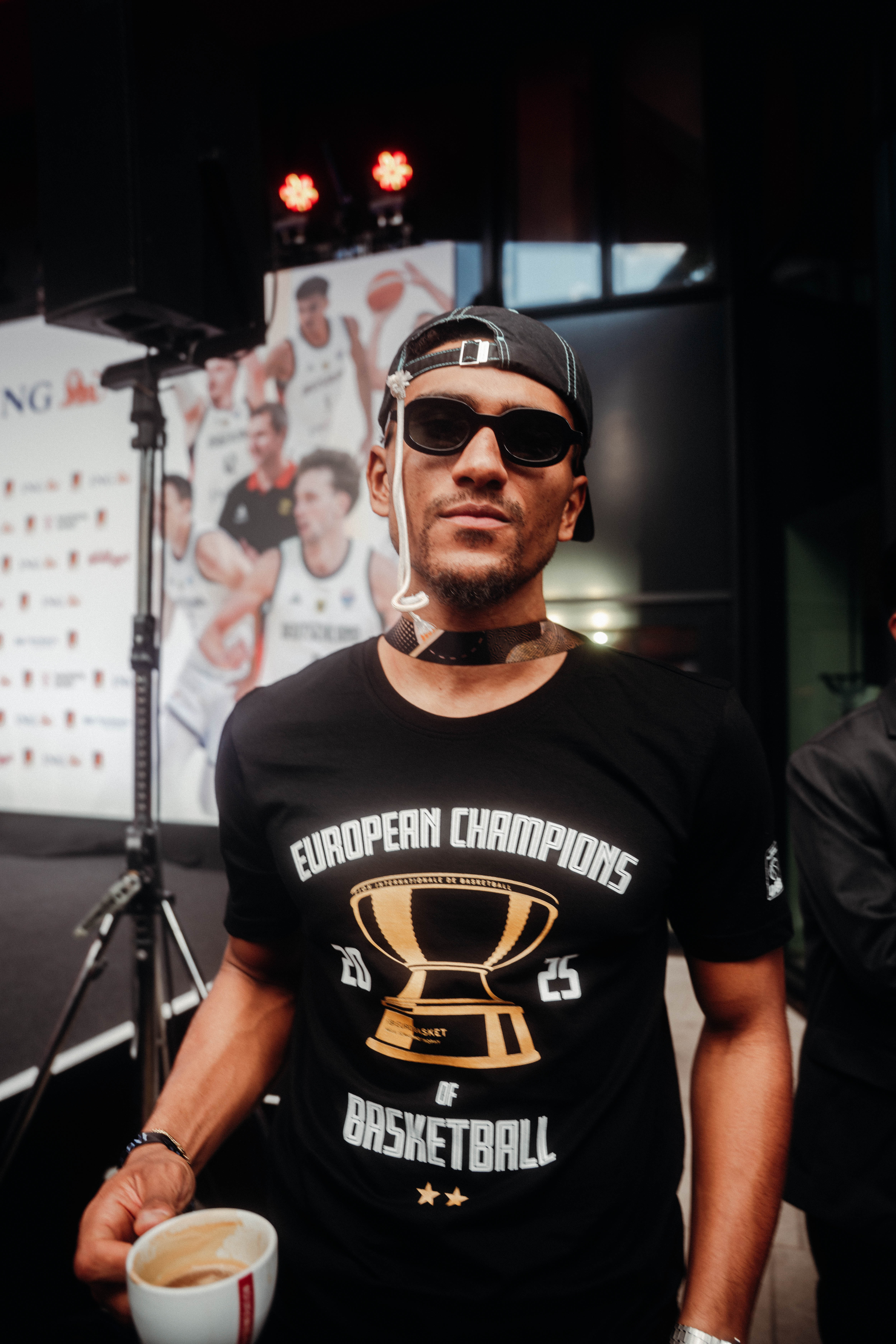 Das Bild zeigt einen Basketballspieler, die ein schwarzes T-Shirt mit dem Aufdruck 'European Champion 2025 of Basketball' trägt.